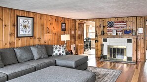 Una sala de estar con un sofá modular, paredes de madera, una chimenea y una bandera estadounidense.