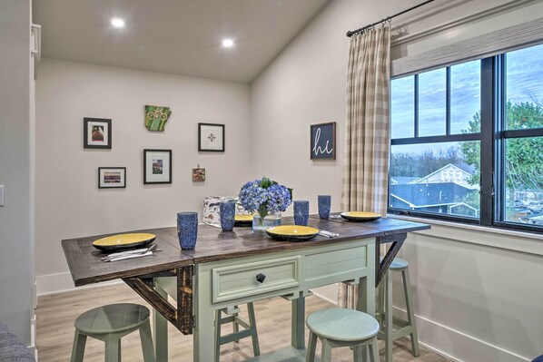 A dining area with a wooden table, blue and yellow plates, and a window with a view of houses.