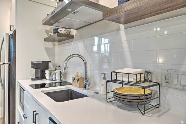 Una cocina moderna con cafetera espresso integrada, un lavamanos de acero inoxidable y un estante de madera sobre la encimera.