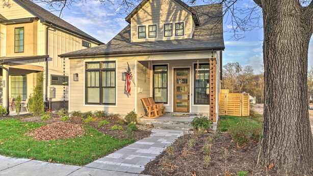 A two-story house with a front porch, a flag, and a wooden bench.