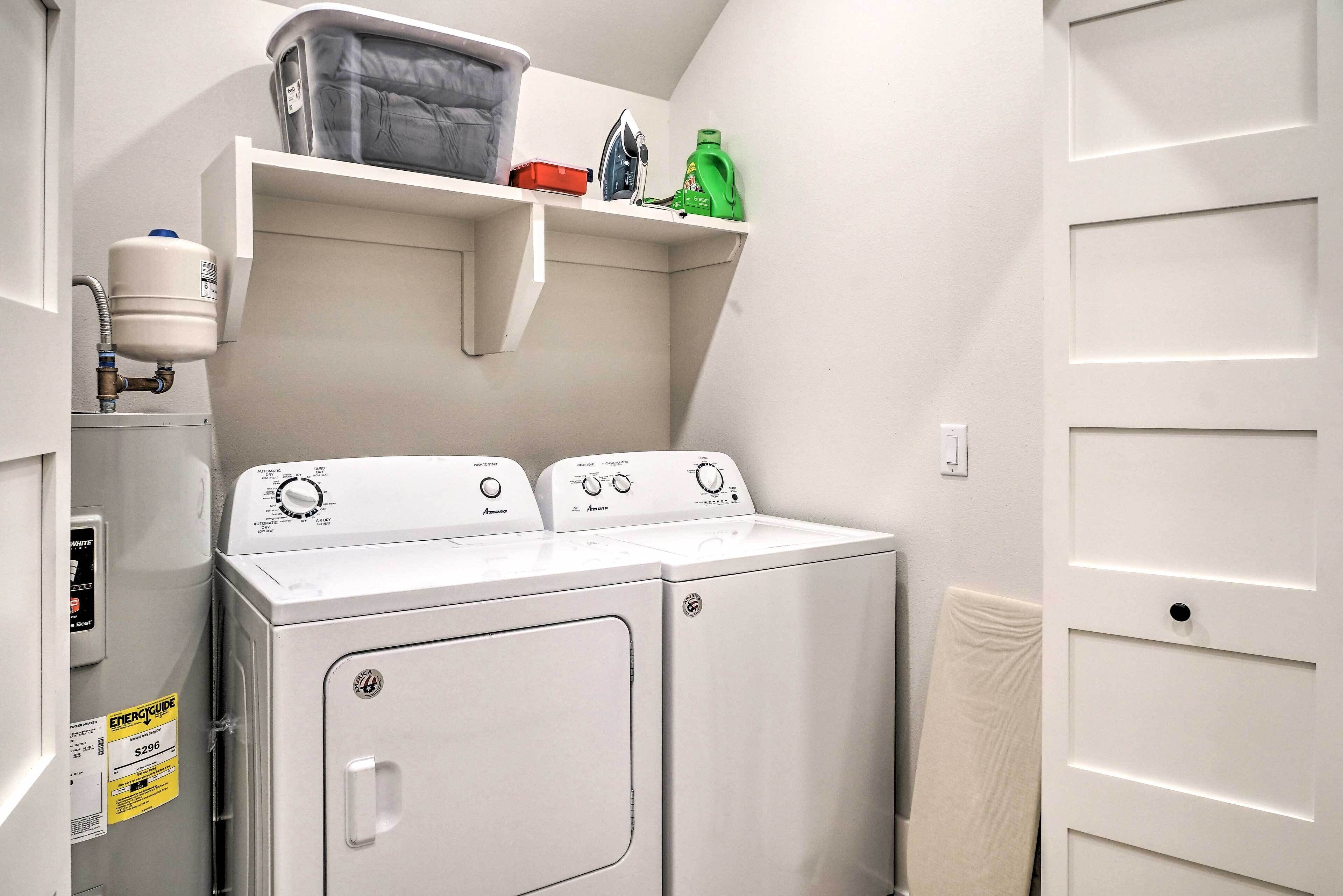 A laundry room with a front-loading washer and dryer, a water heater, and a shelf with laundry supplies.