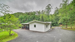 A small, single-story cabin with a porch, surrounded by lush greenery and a forested hillside. - 'creekside Ranch' w/ Porch ~ 2 Mi to Pkwy (Pigeon Forge)