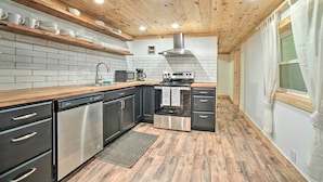 A modern kitchen with black cabinets, stainless steel appliances, wooden shelves, and a tiled backsplash. - 'creekside Ranch' w/ Porch ~ 2 Mi to Pkwy (Pigeon Forge)