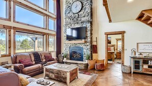 Una sala de estar acogedora con chimenea de piedra, sofá de cuero y un gran ventanal con vistas a un paisaje pintoresco.