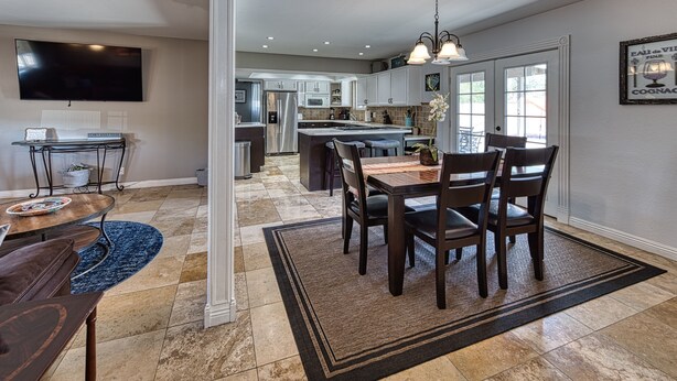 A modern kitchen with stainless steel appliances, a dining area with a wooden table and chairs, and a large TV mounted on the wall. - UPDATED Shasta FUN, Pool & Putting Green, sleeps 11 (Lake Havasu City)