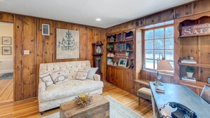 A cozy living room with a wooden paneled wall, a tufted sofa, a bookshelf, and a vintage telephone.