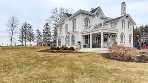 A large, white, two-story house with a wrap-around porch, surrounded by a well-maintained lawn and trees.
