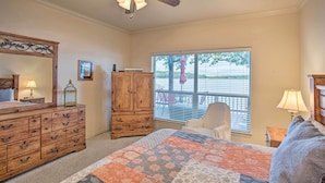 Une chambre à coucher avec un grand lit, une commode en bois, un ventilateur de plafond et une fenêtre avec des stores.