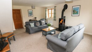 A living room with a grey sofa, a wooden coffee table, a fireplace, and a door in the background. - Ty Rhosyn (Haverfordwest)