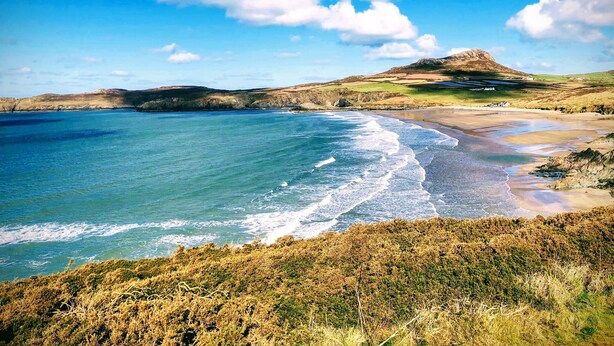 A coastal landscape with a beach, cliffs, and a hill in the background. - Ty Rhosyn (Haverfordwest)