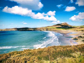 Un paysage côtier avec une plage, des falaises et une colline en arrière-plan.