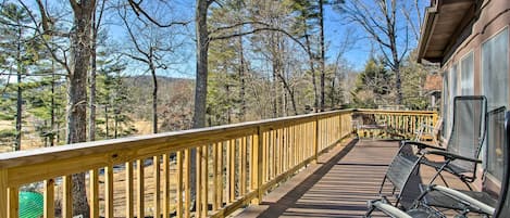 A wooden deck with a railing, outdoor seating, and a view of trees and hills.