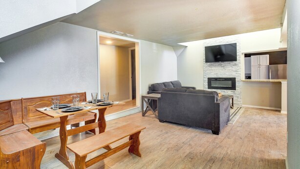 A modern living room with a wooden dining table, benches, a gray sofa, and a fireplace. - Updated Buffalo Springs House on the Lake! (Lubbock)
