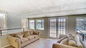 A spacious living room with a beige sofa, a wooden floor, and large windows offering a view of the outdoors. - Updated Buffalo Springs House on the Lake! (Lubbock)