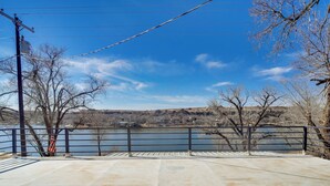 A concrete deck with a railing overlooking a body of water, trees, and distant buildings. - Updated Buffalo Springs House on the Lake! (Lubbock)