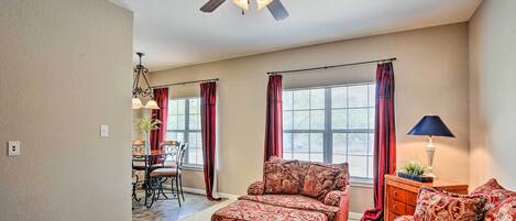 A spacious living room with a ceiling fan, a dining area with a chandelier, and a view through large windows.