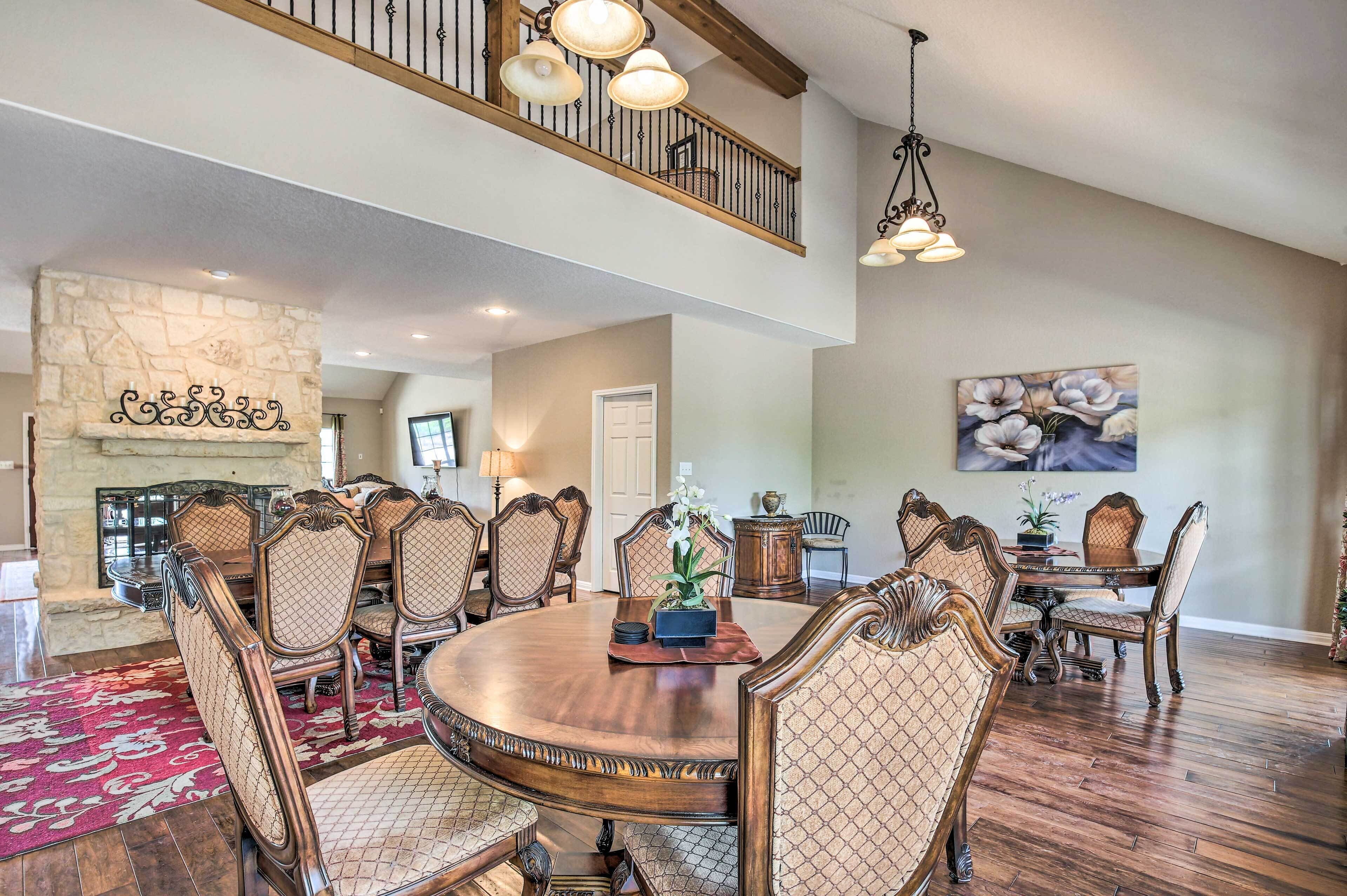 A spacious dining area with a large round table, ornate chairs, and a stone fireplace.