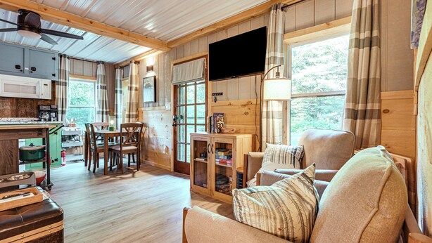 A cozy cabin interior with a dining area, a sofa, a television, and a kitchen with wooden cabinets and a microwave. - Lake Access & Kayaks: Gladwin Cottage Near Golfing (Gladwin)