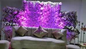 Un sofá con tres cojines en una habitación con un fondo floral y una lámpara decorativa.