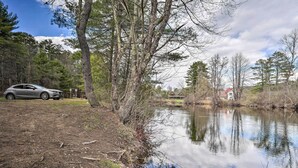 Un coche aparcado cerca de un lago, con árboles y una casa al fondo.
