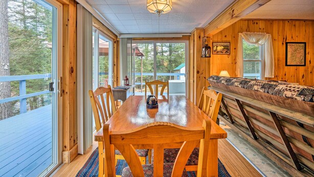 Interior de madera con una mesa y sillas de comedor, un banco y grandes ventanas que ofrecen vistas al exterior.