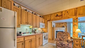 Una cocina con armarios de madera, un refrigerador, un microondas y una estufa. Hay una silla con una manta y una lámpara.