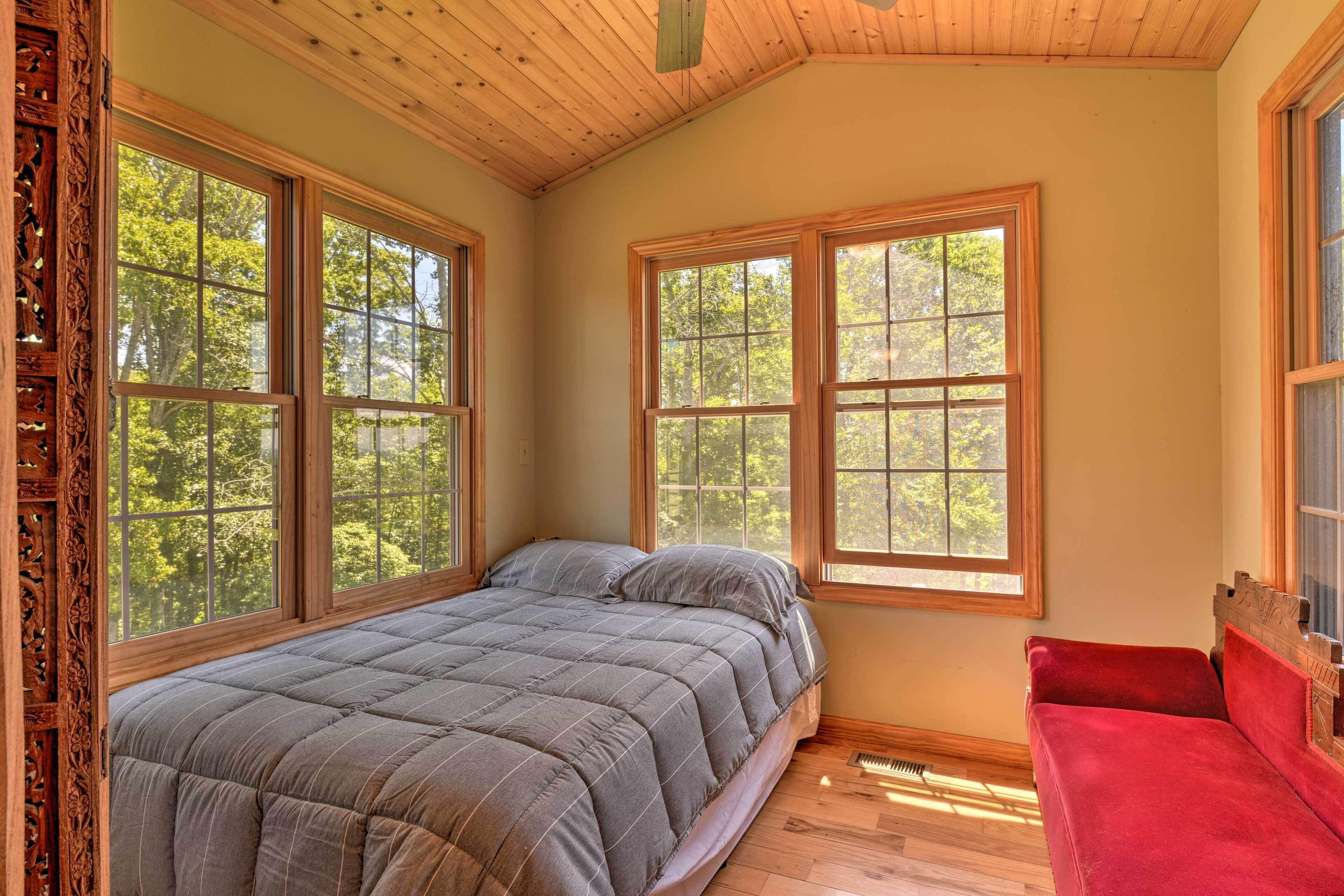 A bedroom with a large bed, two windows, a red chair, and wooden ceiling beams.