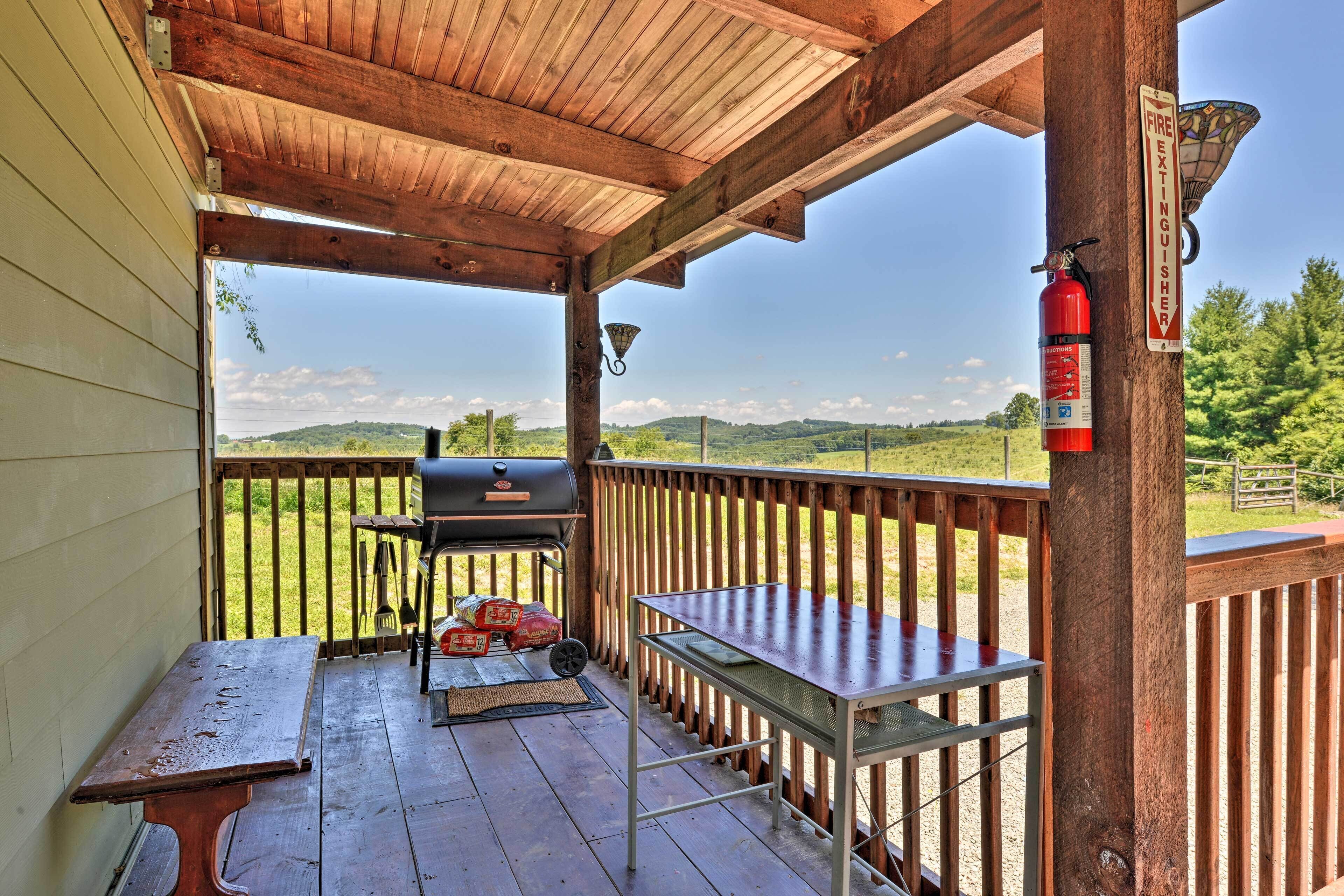 A covered outdoor deck with a barbecue grill, a fire extinguisher, and a view of the countryside.