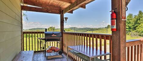 A covered outdoor deck with a barbecue grill, a fire extinguisher, and a view of the countryside.