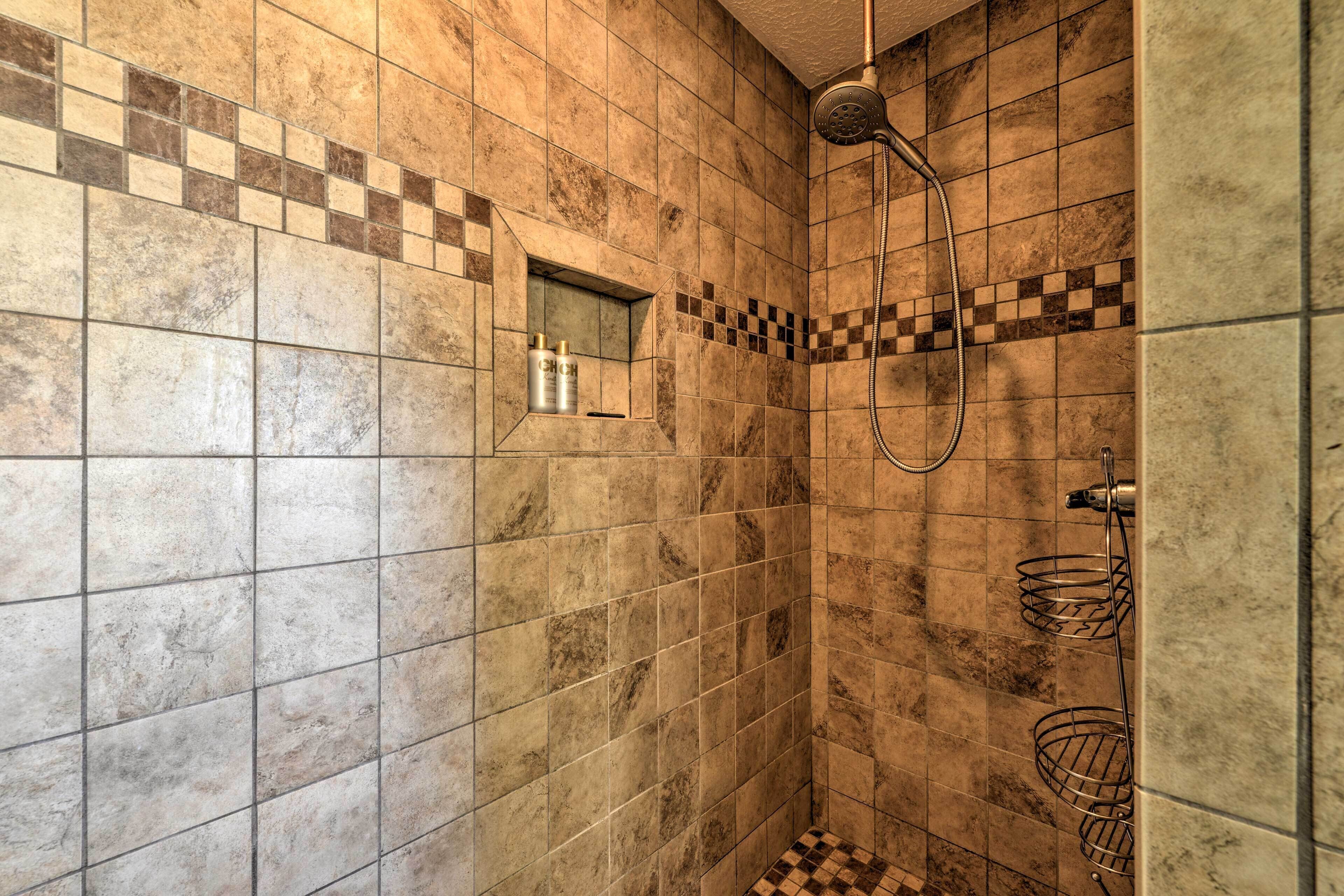 A bathroom with tiled walls, a shower area, and a small shelf with toiletries.