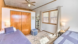 A bedroom with two beds, a ceiling fan, a window with curtains, a bookshelf, and a small stool. - Walk to White River: Home w/ Deck in Flippin! (Flippin)
