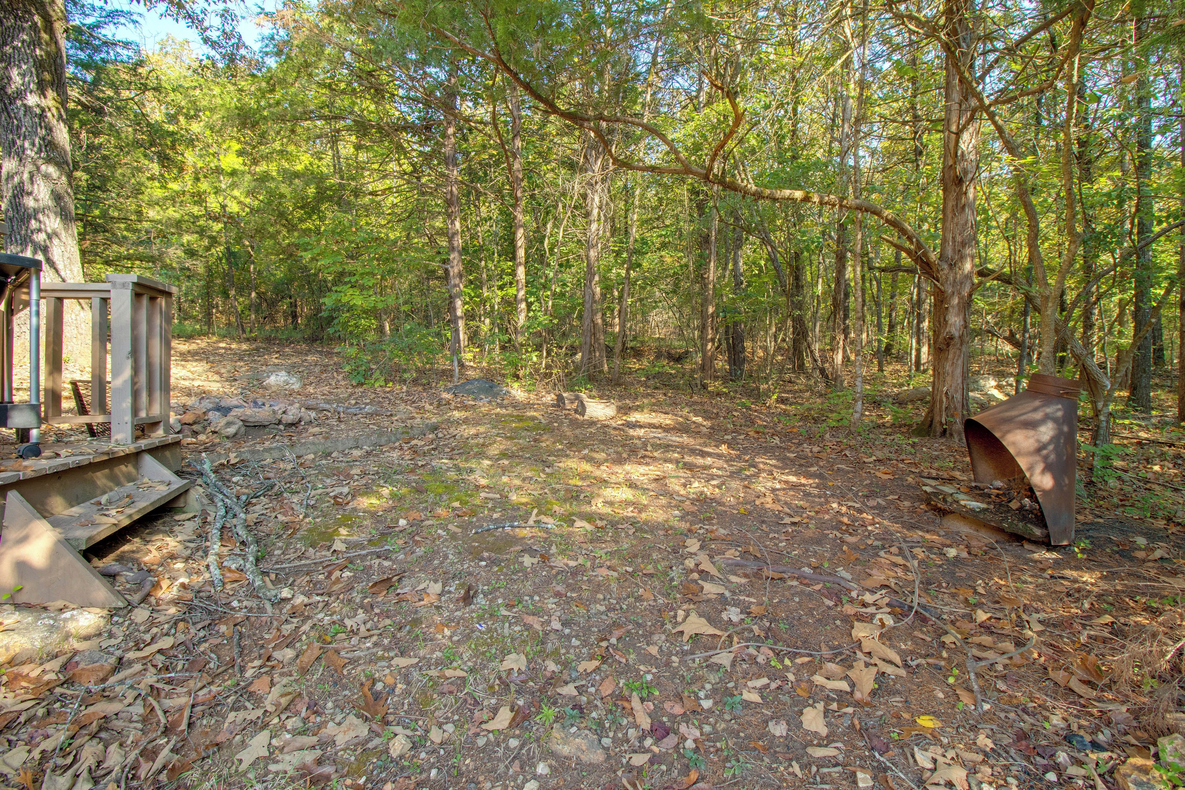 A forested campsite with a metal bench and a small structure.