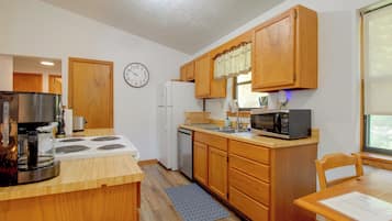 Una cocina compacta con armarios de madera, estufa, refrigerador, microondas y un reloj en la pared.