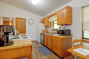 A compact kitchen with wooden cabinets, a stove, a refrigerator, a microwave, and a clock on the wall. - Walk to White River: Home w/ Deck in Flippin! (Flippin)