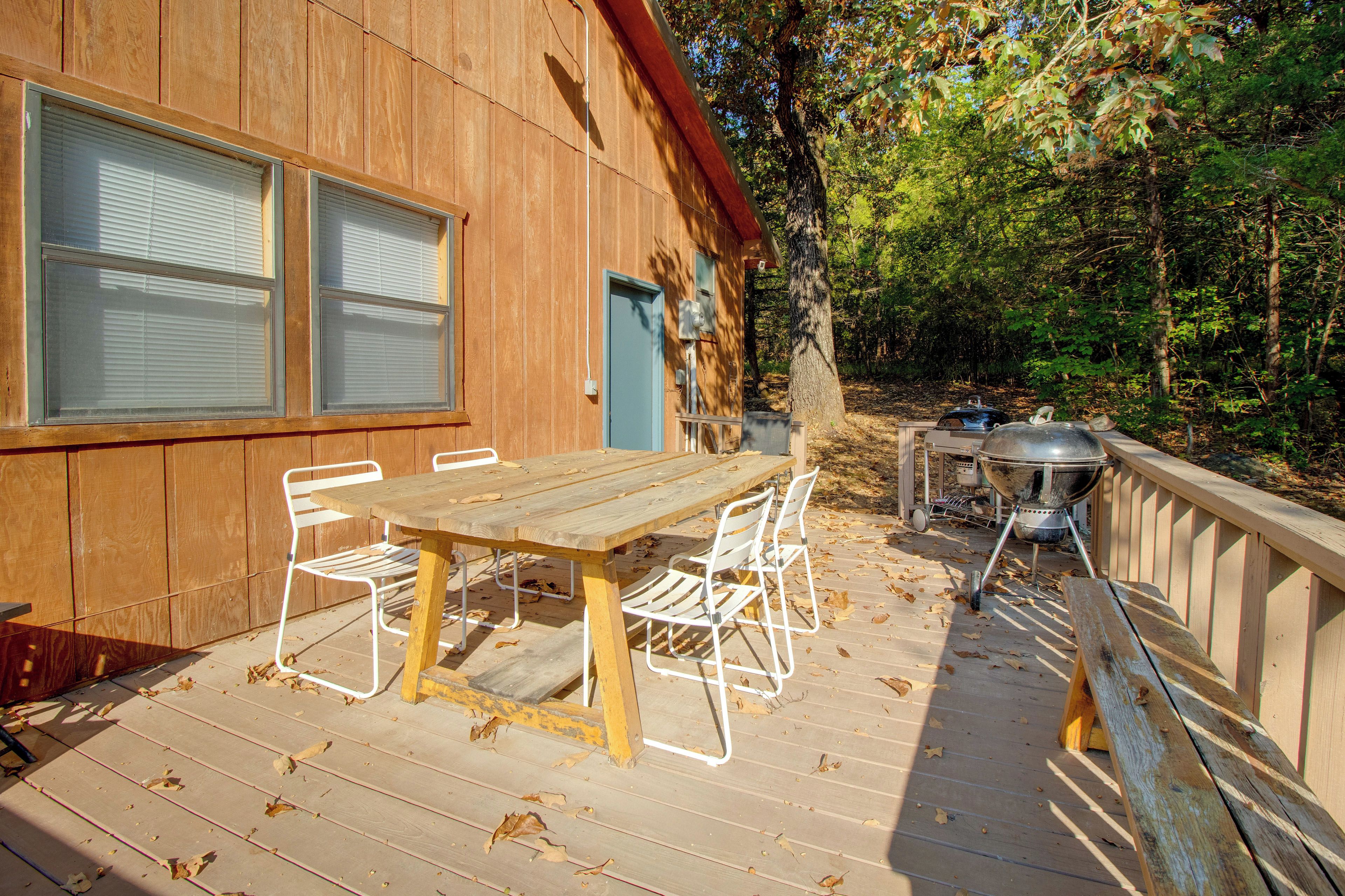 Una terraza de madera con una mesa y sillas, una parrilla y una construcción de madera con ventanas.