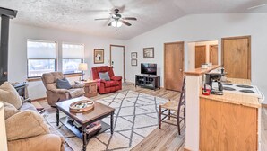 A living room with a fireplace, a TV, and a kitchen area with a stove and coffee maker. - Walk to White River: Home w/ Deck in Flippin! (Flippin)