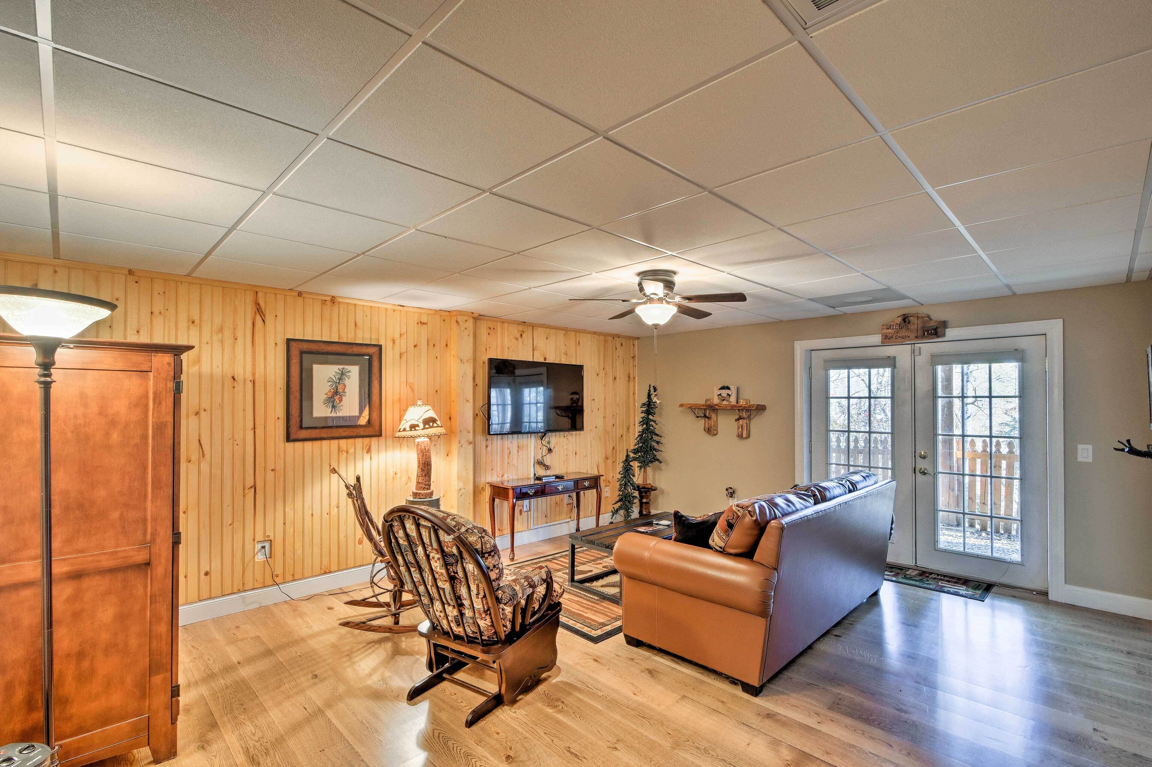 A spacious living room with wooden walls, a ceiling fan, a leather sofa, a rocking chair, and a television.