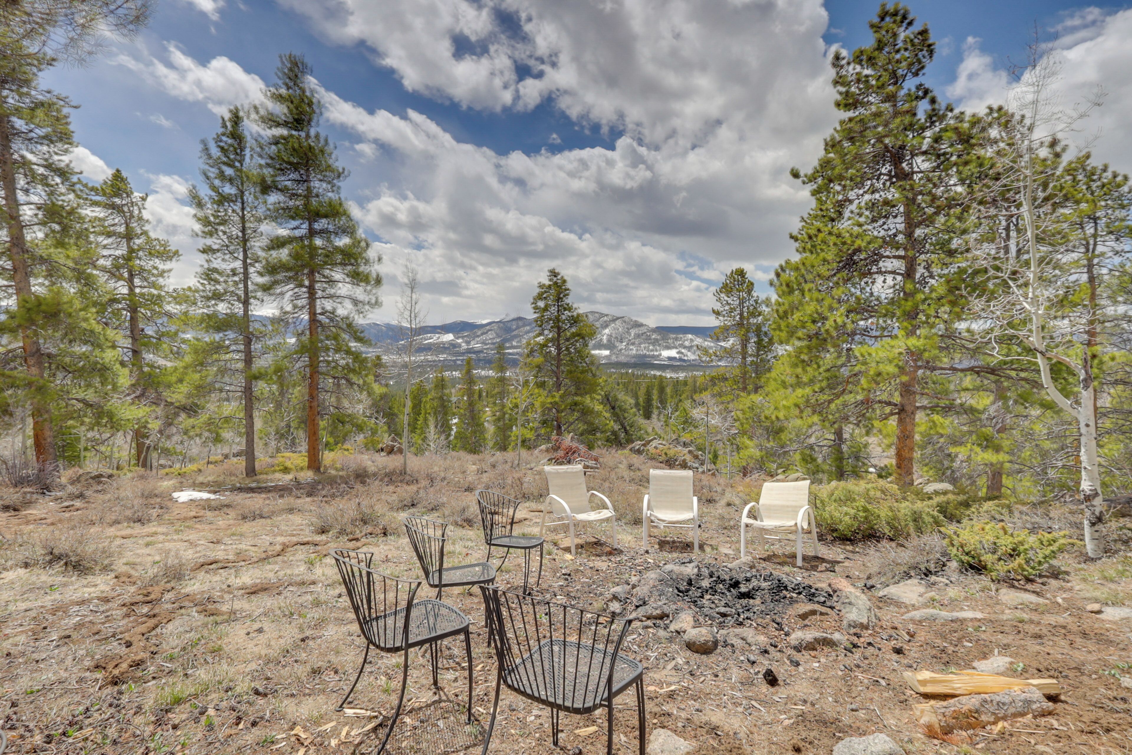 A rustic outdoor seating area with metal chairs and a table, surrounded by trees and a mountainous backdrop.