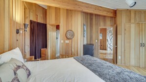 Une chambre à coucher aux murs lambrissés, comprenant un lit, une commode, un miroir et une porte donnant sur une autre pièce.