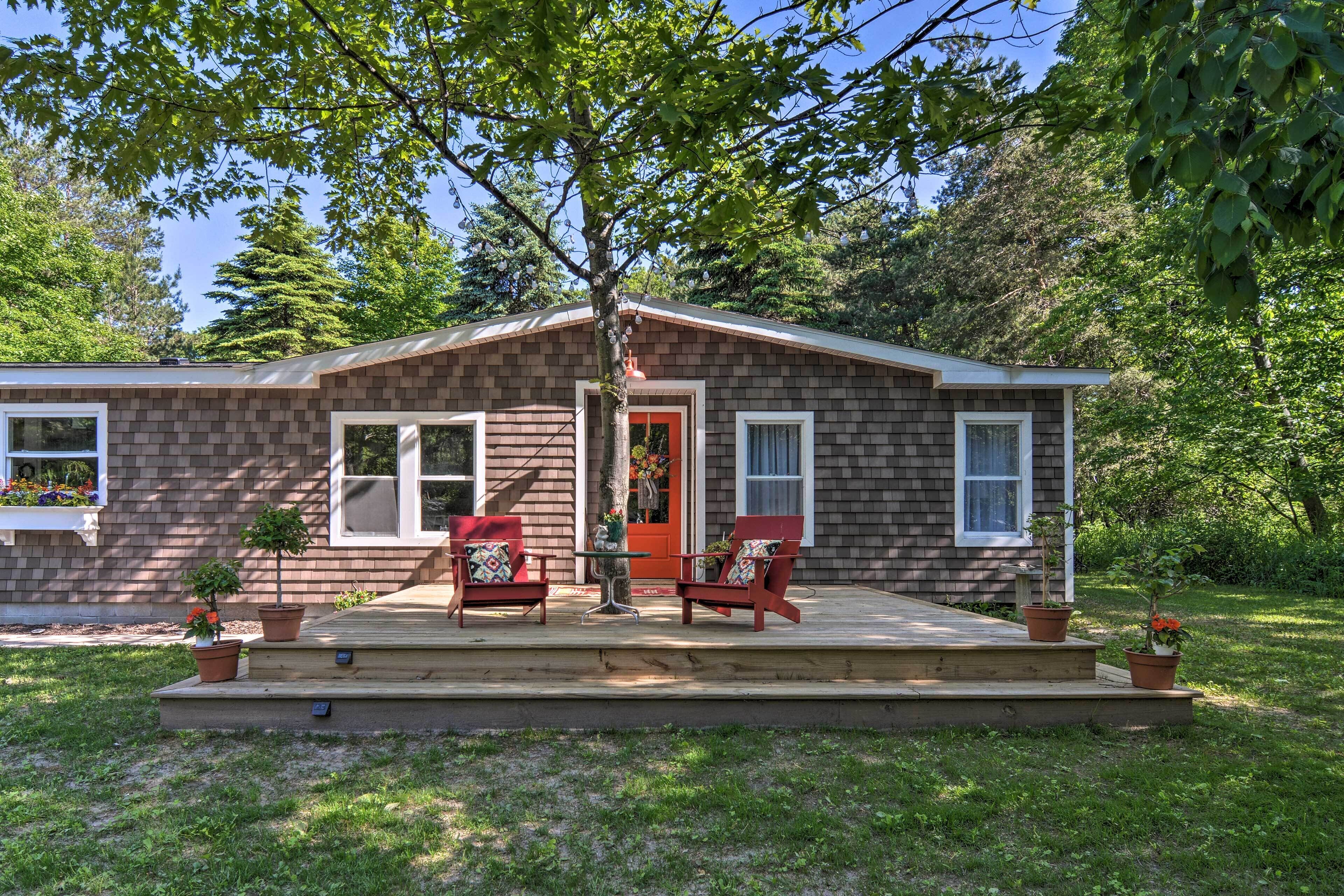 A two-story house with a front porch, two red chairs, and potted plants.