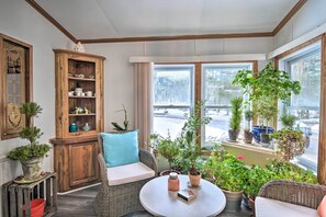 Um canto aconchegante com um sofá de vime, um armário de madeira com jogos de chá e diversas plantas em vasos.