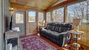 A cozy room with a wooden ceiling, a large window, a sofa, a lamp, and a fireplace. - Cozy Log Cabin: 6 Mi to Great Smoky Mtns NP! (Townsend)