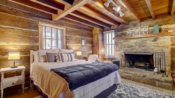 A log cabin bedroom with a stone fireplace, wooden beams, and a bed with a blue blanket. - Cozy Log Cabin: 6 Mi to Great Smoky Mtns NP! (Townsend)