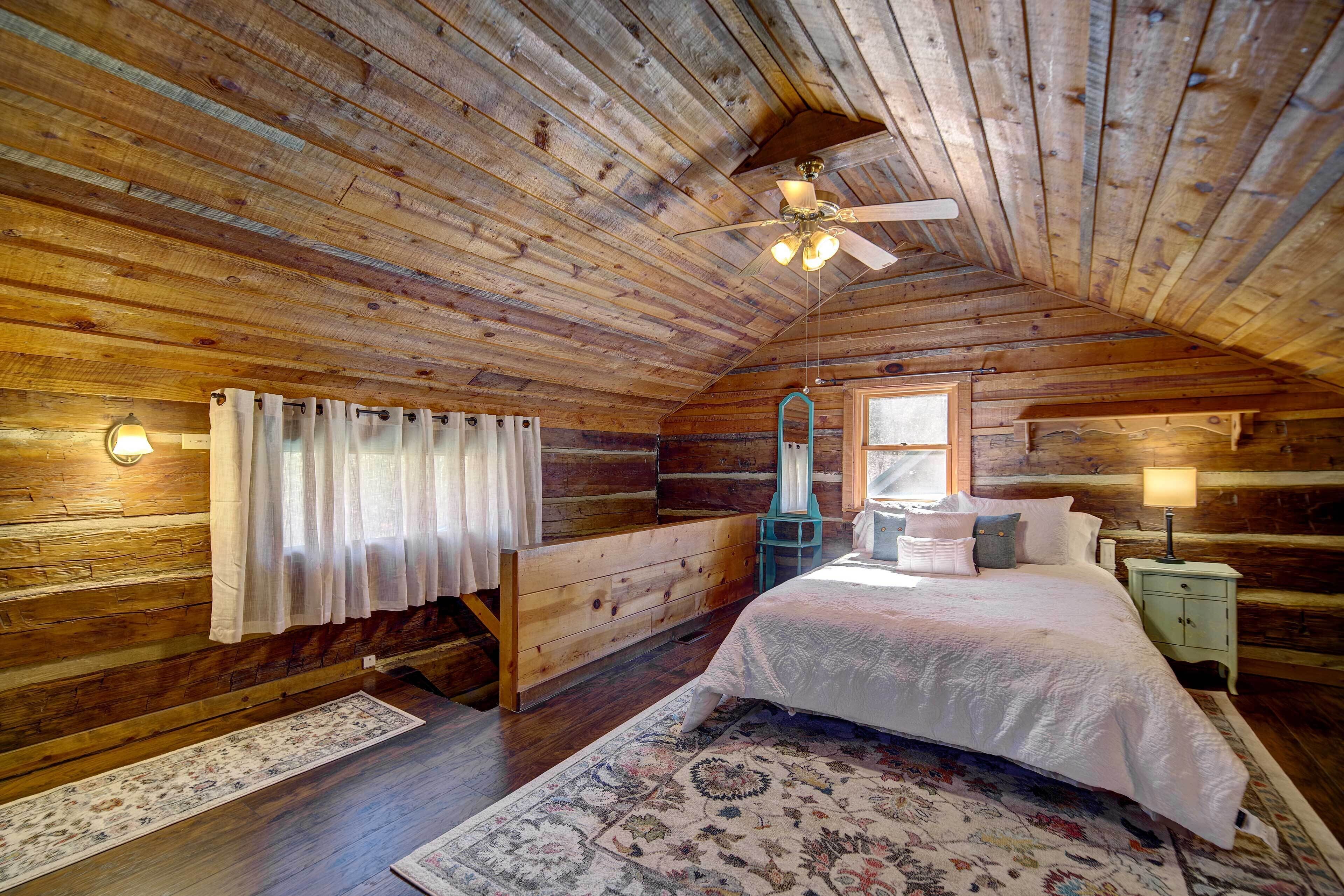 Ein gemütliches Schlafzimmer in einer Blockhütte mit Holzboden, einem Bett mit weißer Bettwäsche, einem Nachttisch und einem Fenster mit Vorhängen.