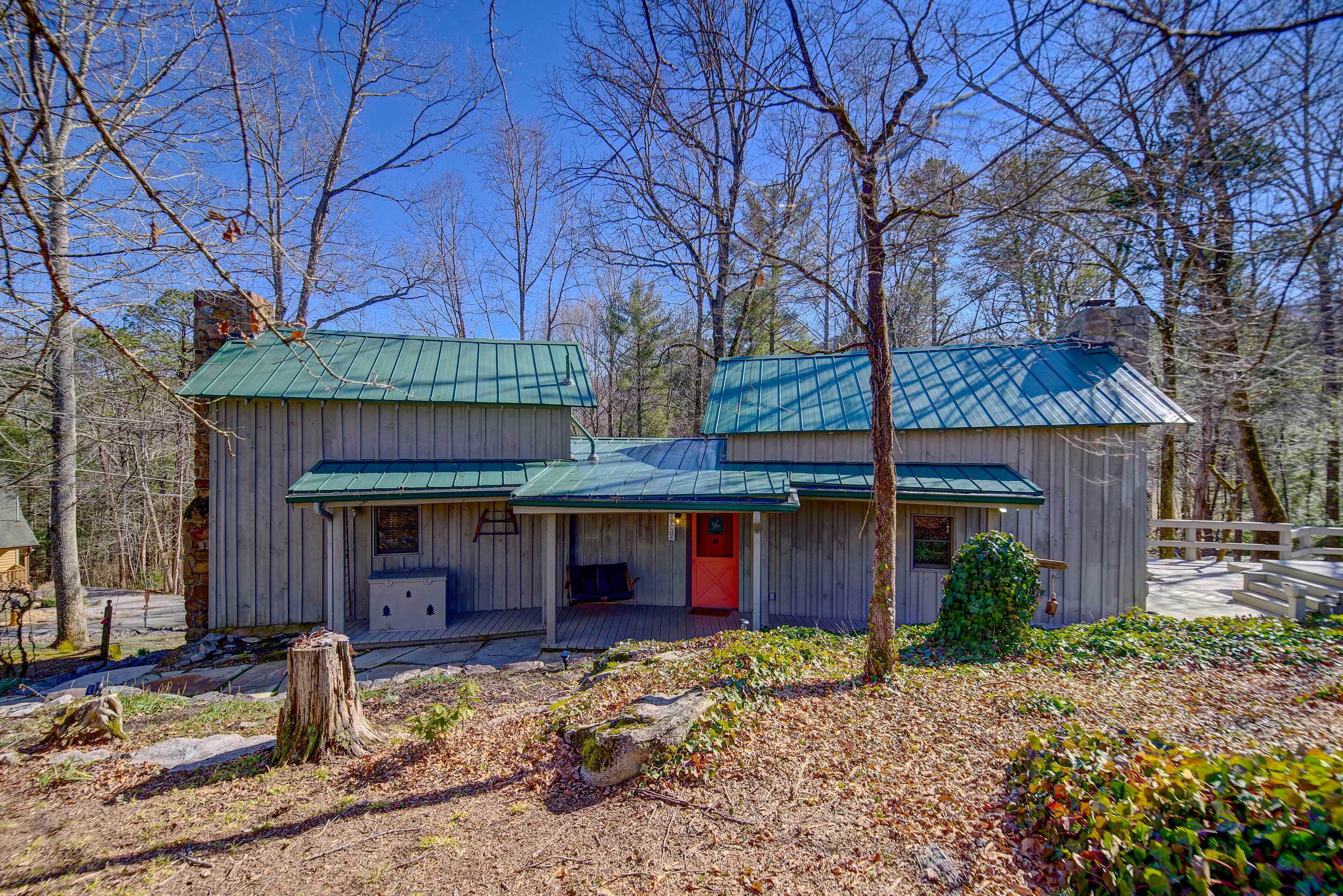 A rustic cabin with a green roof, a red door, and a porch with a bench.