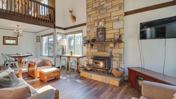 A cozy living room with a stone fireplace, wooden furniture, and a balcony with a deer head decoration. - Near Skiing: Lakefront Gem w/ Kayaks in Long Pond (Long Pond)