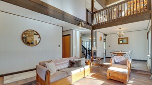 A spacious living area with a wooden sofa and armchair, a round mirror, and a staircase leading to an upper level. - Near Skiing: Lakefront Gem w/ Kayaks in Long Pond (Long Pond)
