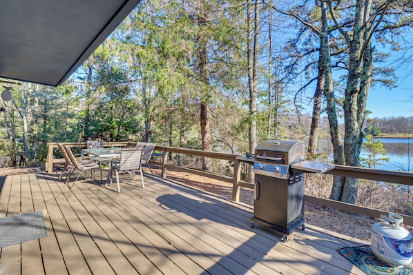 Terraza de madera con una parrilla y zona de estar con vistas a un lago.
