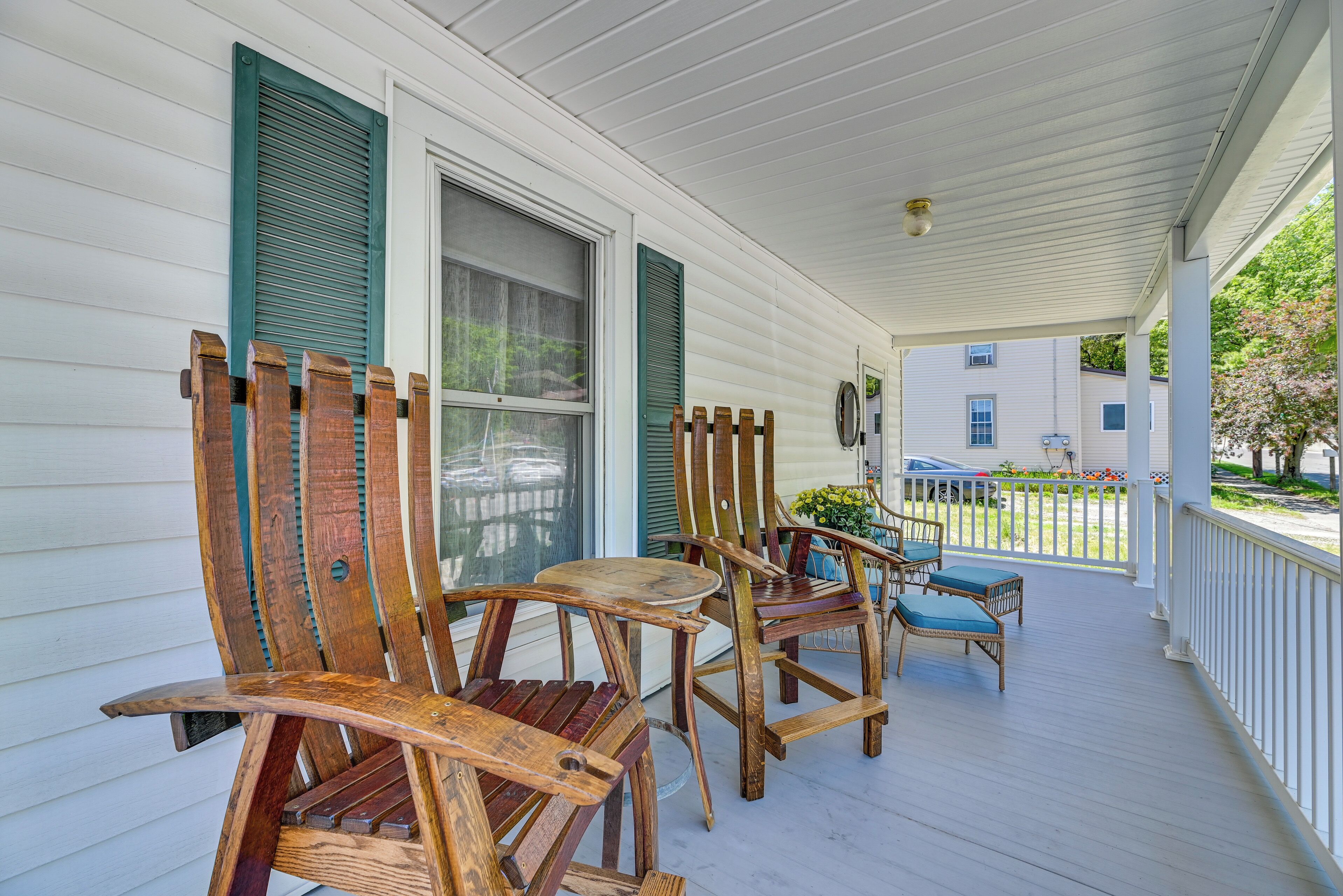 A porch with wooden chairs and a table, white siding, and a view of a neighboring house.