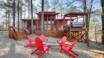 A cabin with a deck, a fire pit, and red Adirondack chairs.